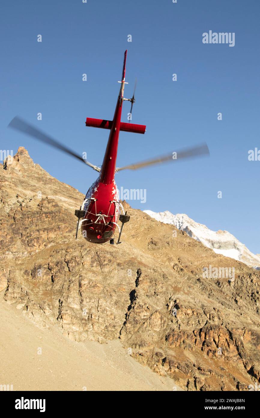 Red Helicopter Landing On A Rugged Mountain Ridge With Snow Capped red-helicopter-landing-on-a-rugged-mountain-ridge-with-snow-capped
