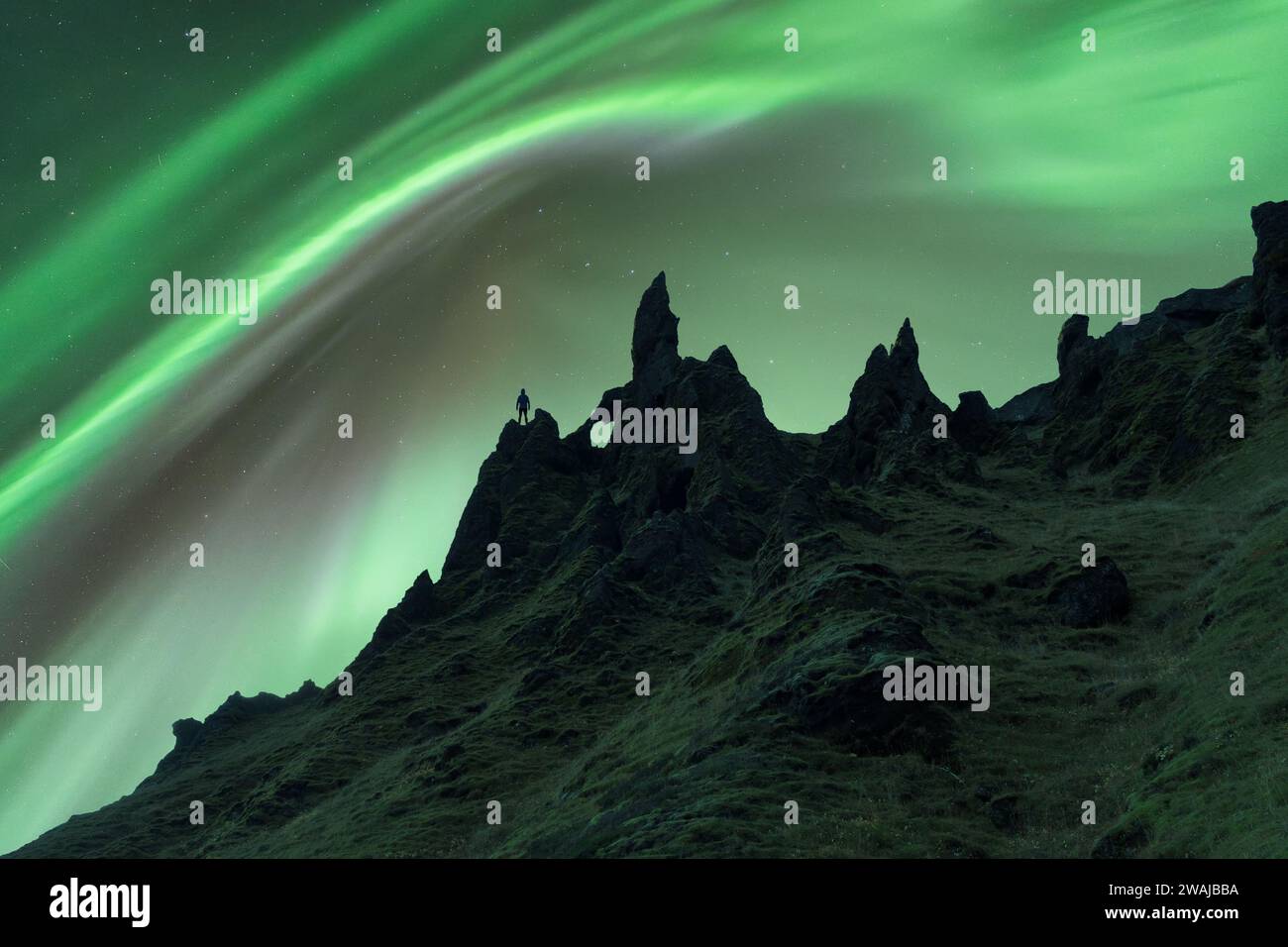 An unrecognizable person's silhouette stands out against jagged rock formations under the aurora borealis in Iceland Stock Photo