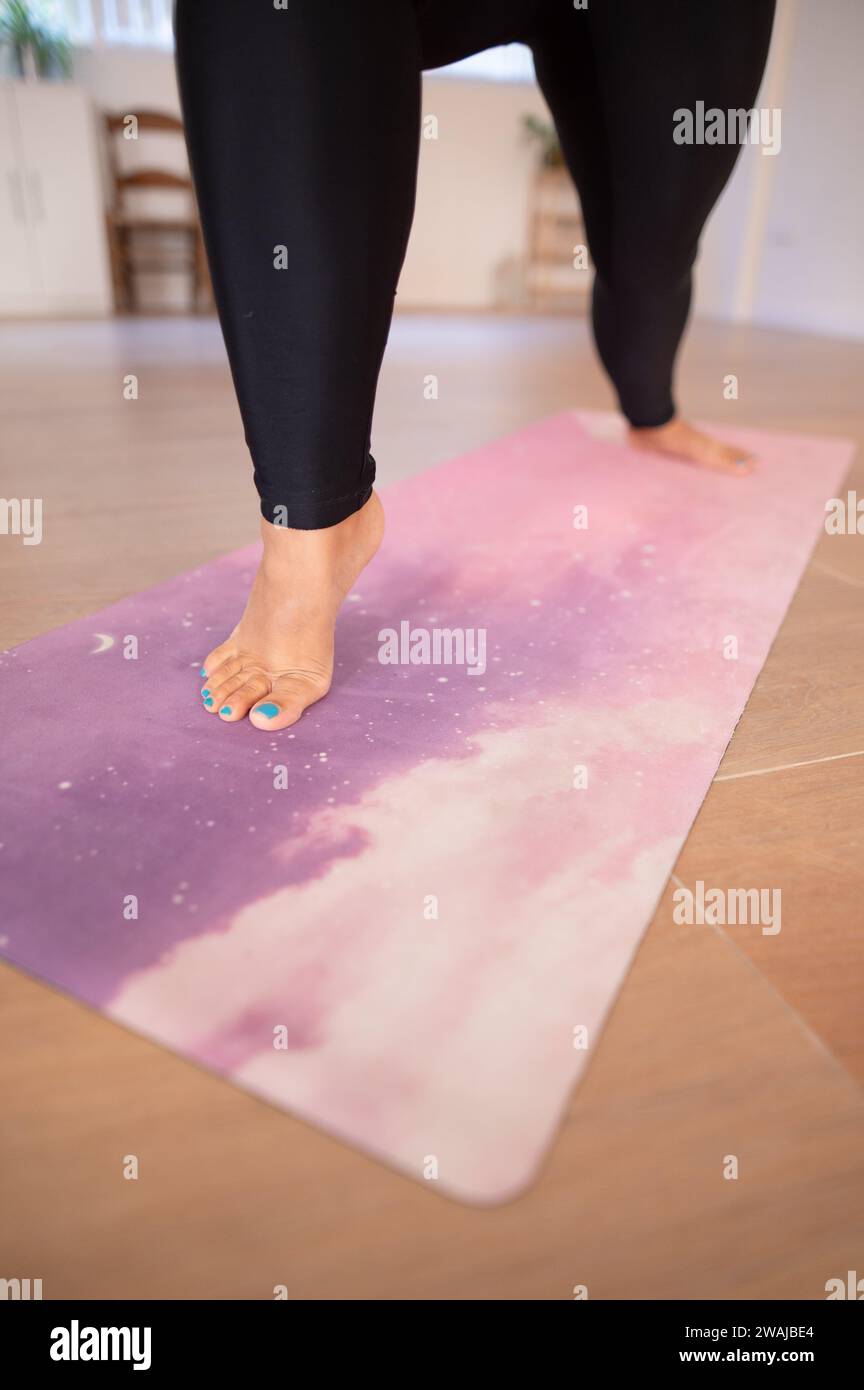 Crop barefooted female in black leggings performing stretching exercise on purple mat during yoga fitness exercise Stock Photo