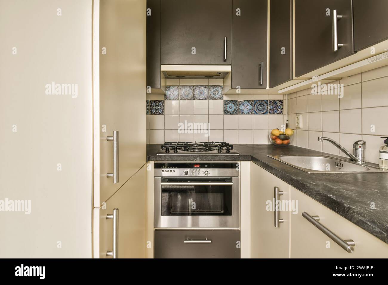 Stainless steel stove with washbasin at black countertop with refrigerator in kitchen with cabinets at home Stock Photo