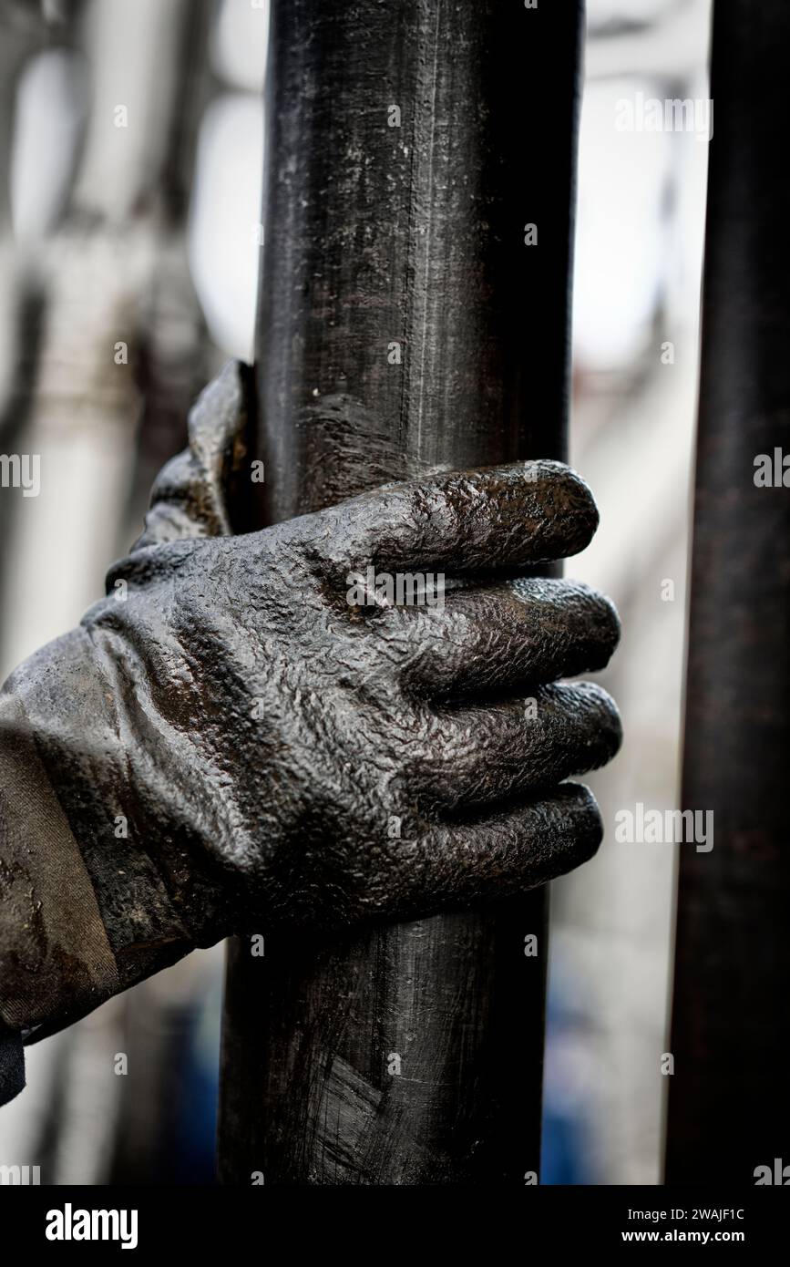 A human hand wearing a pair of gloves on oily drilling pipe Stock Photo