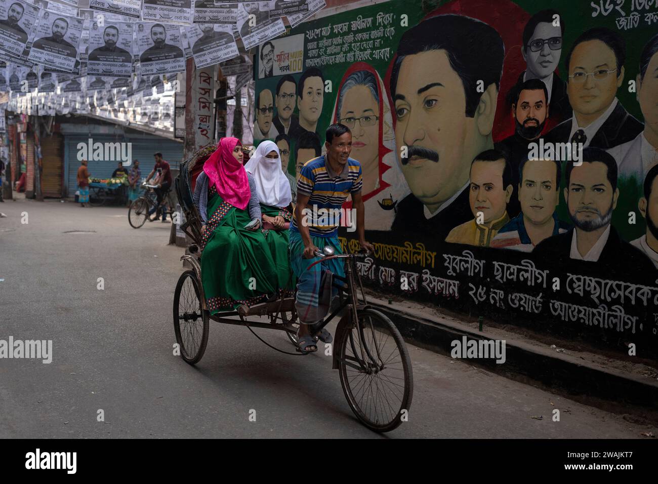 Altaf Rickshwa A rickshaw ferrying passengers rides past a mural displaying portraits ...