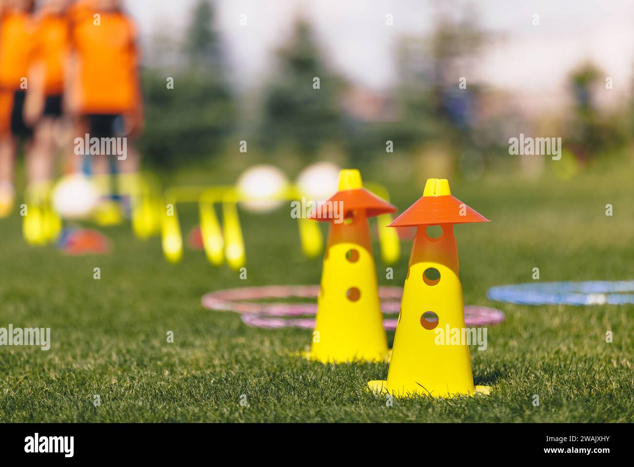 Sports training tools. Soccer equipment on pitch. Yellow and red practice cones on sports field. Children in the background on sports training Stock Photo