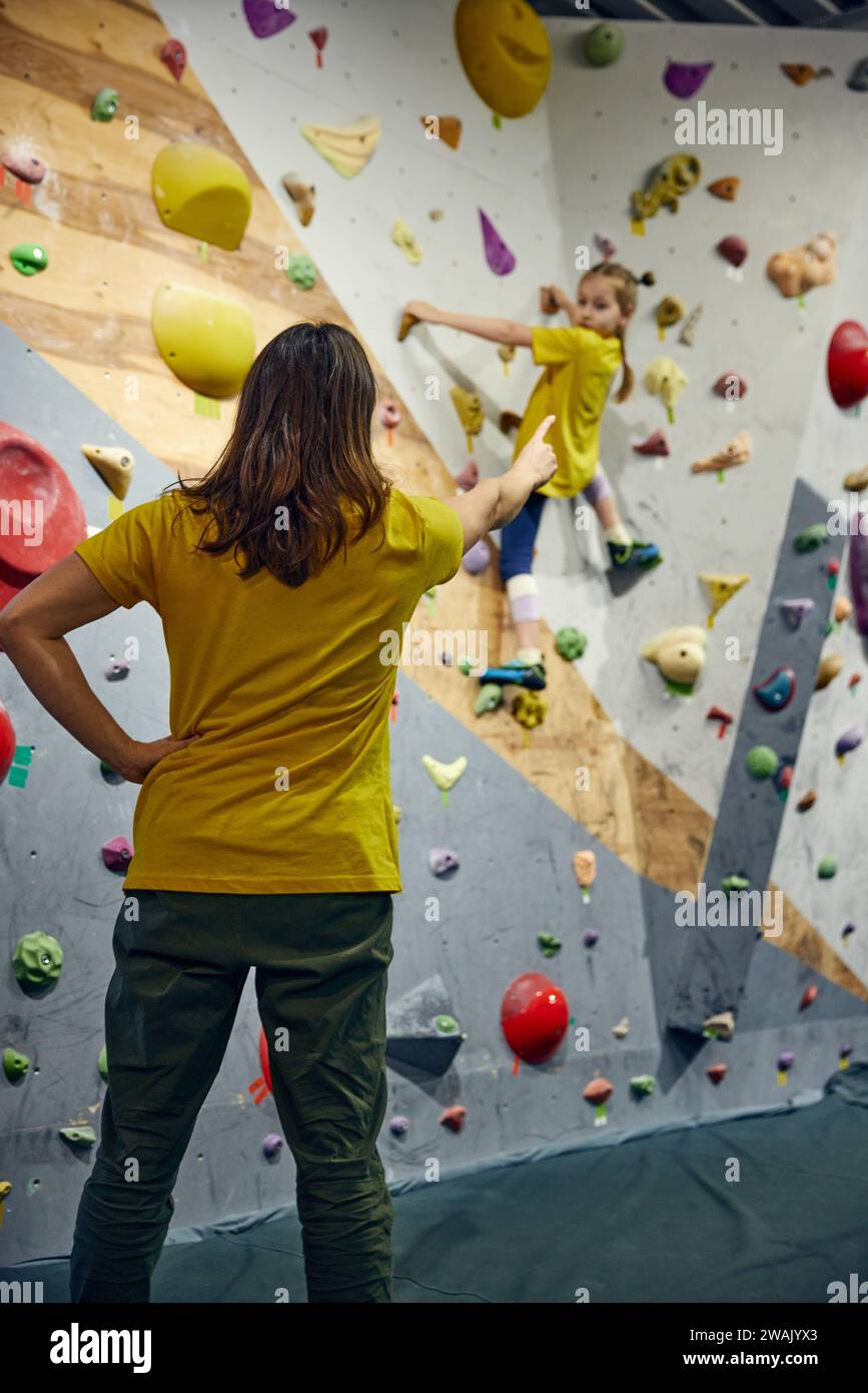 Female bouldering trainer teaching little girl, child bouldering