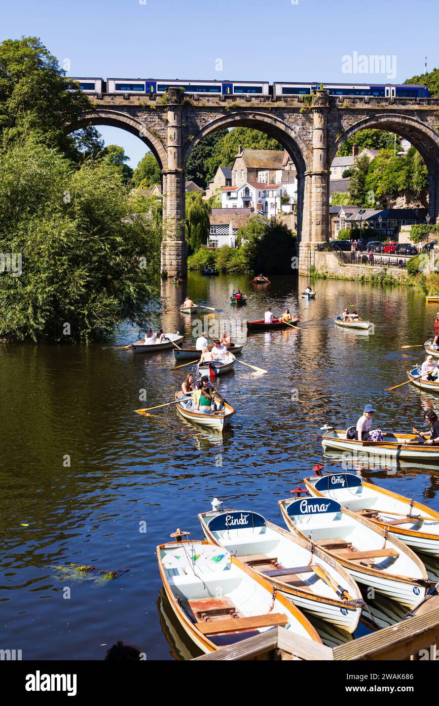 Tourists in hire rowing boats on the River Nidd, with a train passing