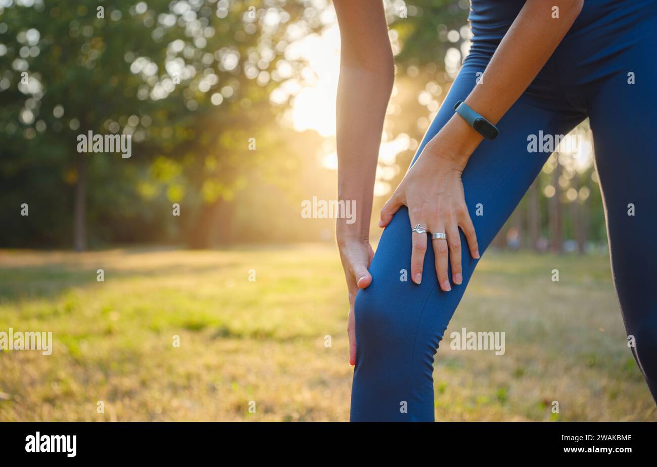 woman with knee pain in evening park. hold her sports injured knee. Low