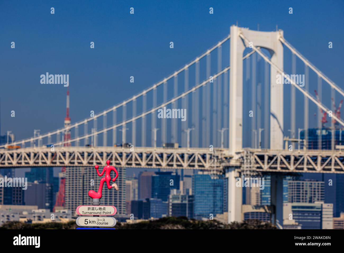 detail of the main span of rainbow bridge in tokyo harbour with a small pink statue of a cartoon runner in foreground marking a running route Stock Photo