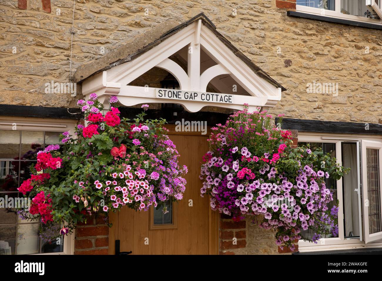 UK, England, Oxfordshire, Fringford, Main Street, Stone Gap Cottage colourful floral hanging baskets Stock Photo