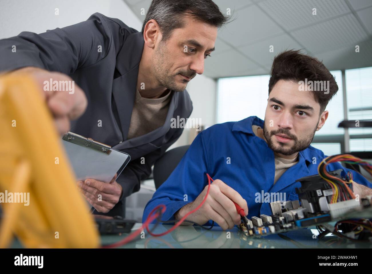 mentor guiding apprentice engineer when using a multimeter Stock Photo