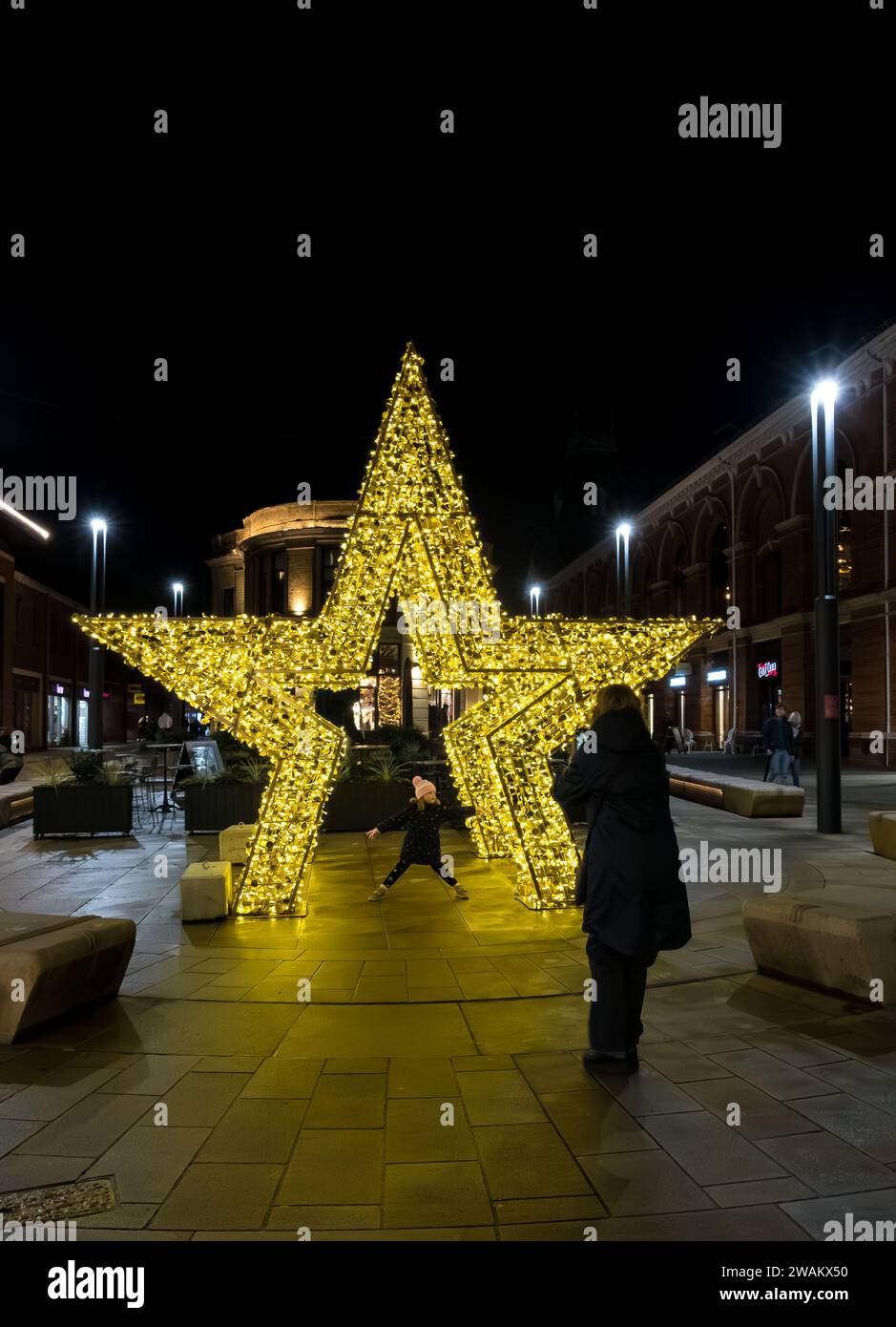woman taking photo on mobile phone of young girl posing under gold star, Cornhill, Lincoln City, Lincolnshire, England, UK Stock Photo