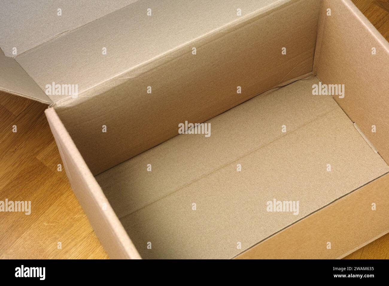 An empty open cardboard box on a wooden floor. Close up. Stock Photo