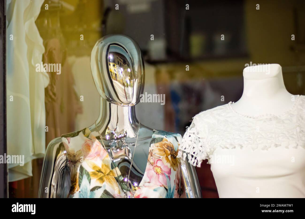 Shiny chrome mannequin dummy standing in a store window display with other mannequins in the