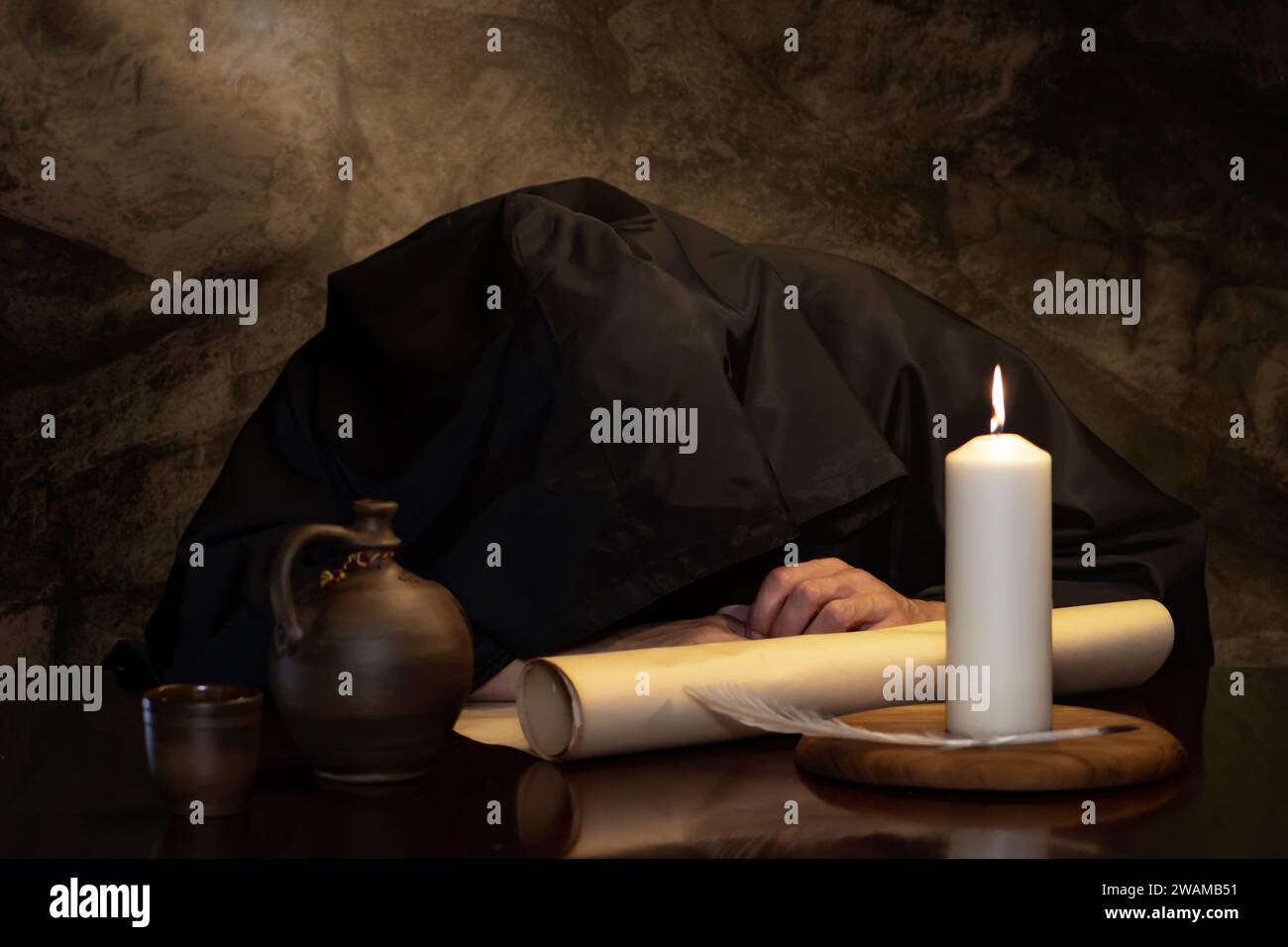 A monk in a black cassock fell asleep drunk at a table with a jug of wine in a medieval coaching inn. Concept: drunkenness and alcoholism. Stock Photo