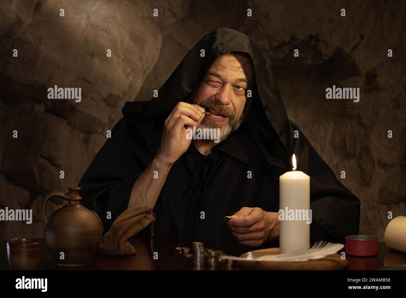 A monk authenticates money by candlelight in a dark stone room, stacks of coins. Concept: tax collector in the Middle Ages, church treasurer. Stock Photo