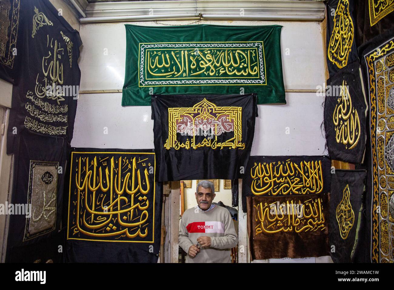 Cairo, Egypt. 05th Jan, 2024. Ahmed Shawki Othman al-Qasbagi, an Egyptian embroiderer whose family has traditionally been responsible for creating the Kiswa, is posing for a photograph next to verses from the Holy Koran that he has sewn onto a replica drape. This drape is available for sale from his workshop gallery in the district of al-Hussein in Islamic Cairo, Egypt, on January 5, 2024. (Photo by Mahmoud Elkhwas/NurPhoto) Credit: NurPhoto SRL/Alamy Live News Stock Photo