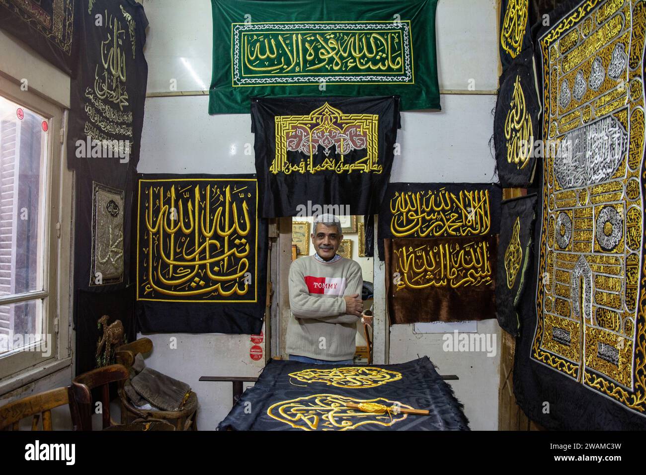 Cairo, Egypt. 05th Jan, 2024. Ahmed Shawki Othman al-Qasbagi, an Egyptian embroiderer whose family has traditionally been responsible for creating the Kiswa, is posing for a photograph next to verses from the Holy Koran that he has sewn onto a replica drape. This drape is available for sale from his workshop gallery in the district of al-Hussein in Islamic Cairo, Egypt, on January 5, 2024. (Photo by Mahmoud Elkhwas/NurPhoto) Credit: NurPhoto SRL/Alamy Live News Stock Photo