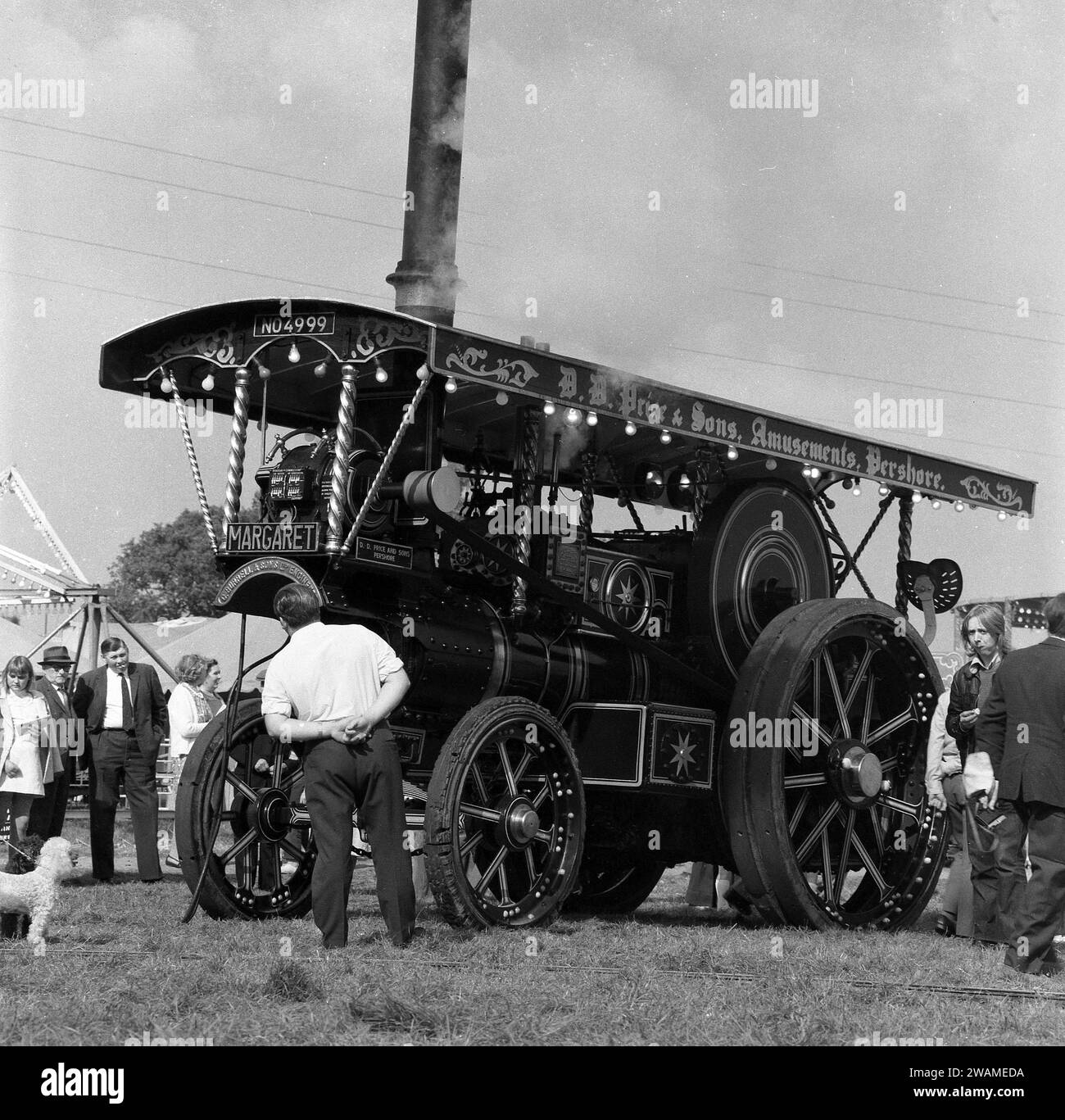 1970, historical, outside at a steam fair, visitors looking at the steam powered tractor, 'Margaret', built in 1922 and known as a Showmans Road Locomotive.  Maker's nameplate on front; C. Burrell & Sons Ltd, England. Number plate is NO 4999. Founded in 1770 and based at Thetford, Norfolk, Charles Burrell & Sons were builders of steam traction engines and related machinery and traded until the late 1920s, when the internal combustion engine became a more effective alternative to steam power. Stock Photo