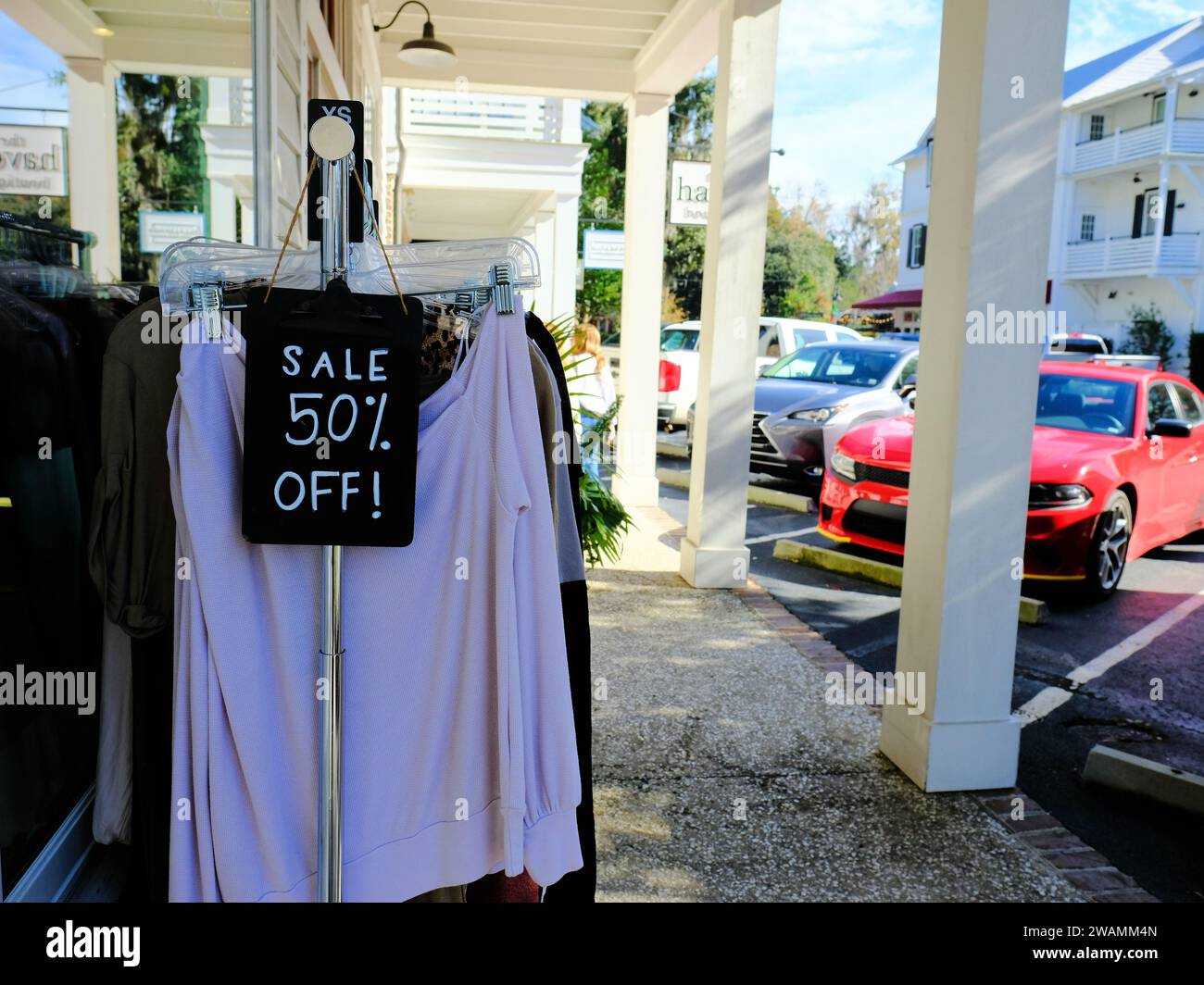 Rack with clothes outdoors on a sidewalk with a Sale 50% Off! sign noting markdown on original price and cost; priced to sell and move merchandise. Stock Photo