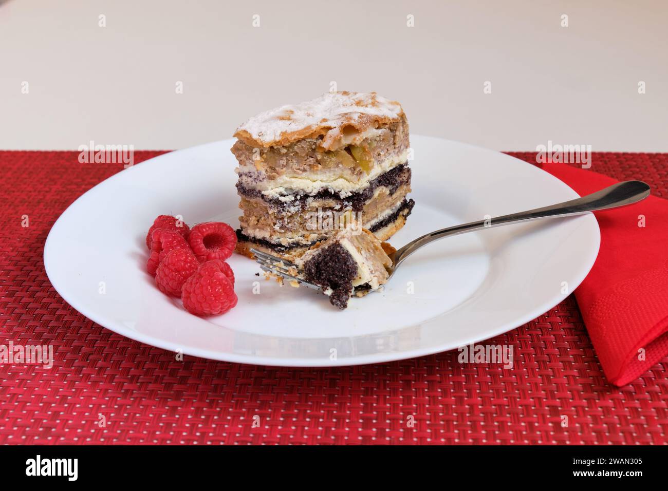 Slovenian tradional layered pastry from province of Prekmurje. (PREKMURSKA GIBANICA).  Cake sits on a white plate with fork and raspberries. Stock Photo