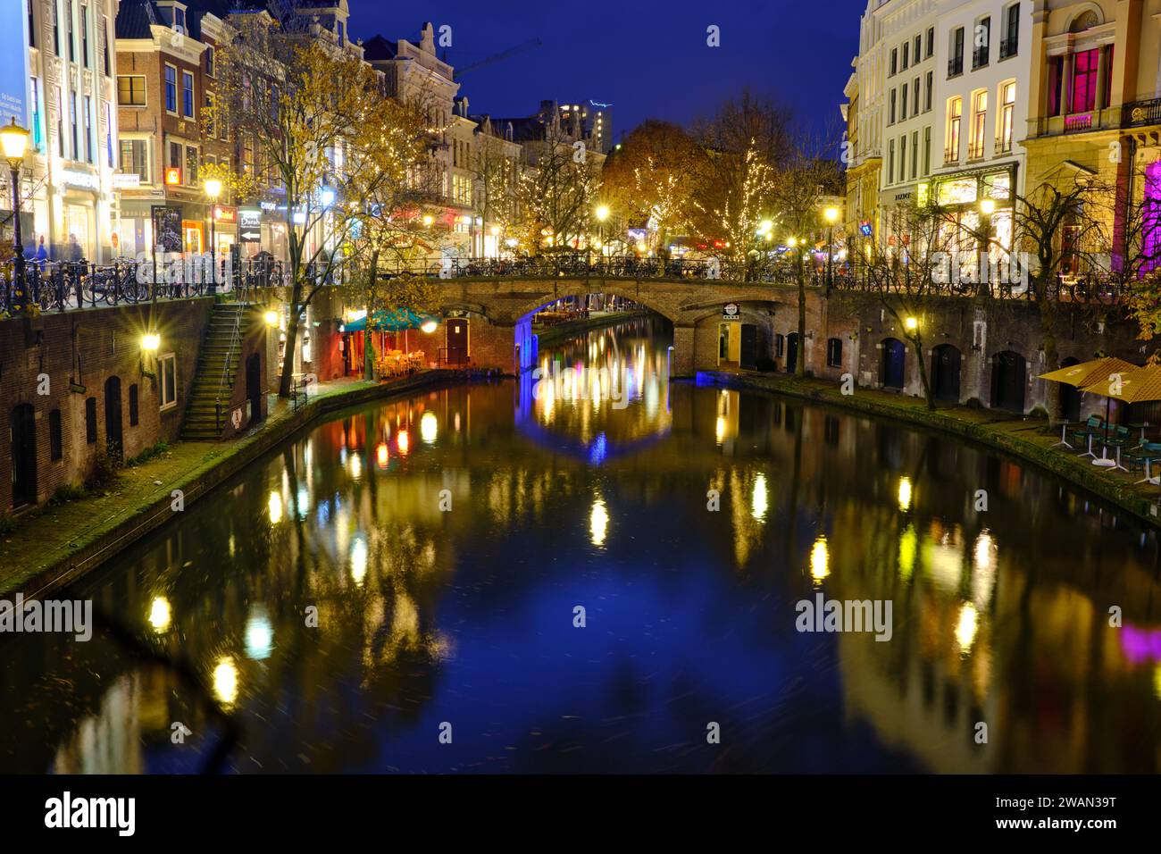 Canal in Utrecht lit up at night with houses, shops and bridge Stock Photo