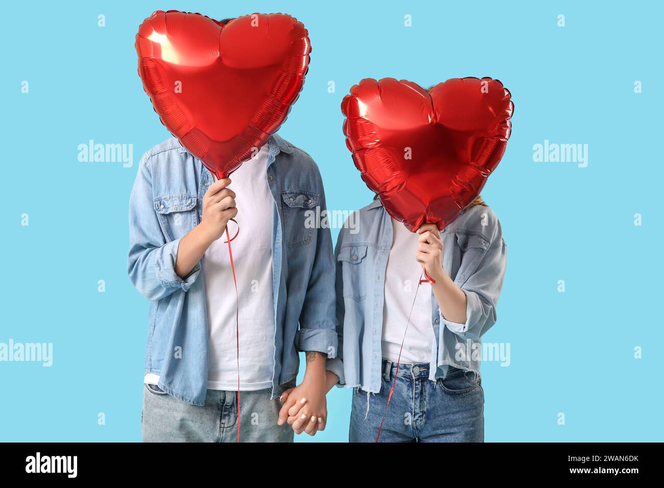Couple with heart-shaped air balloons holding hands on blue background ...