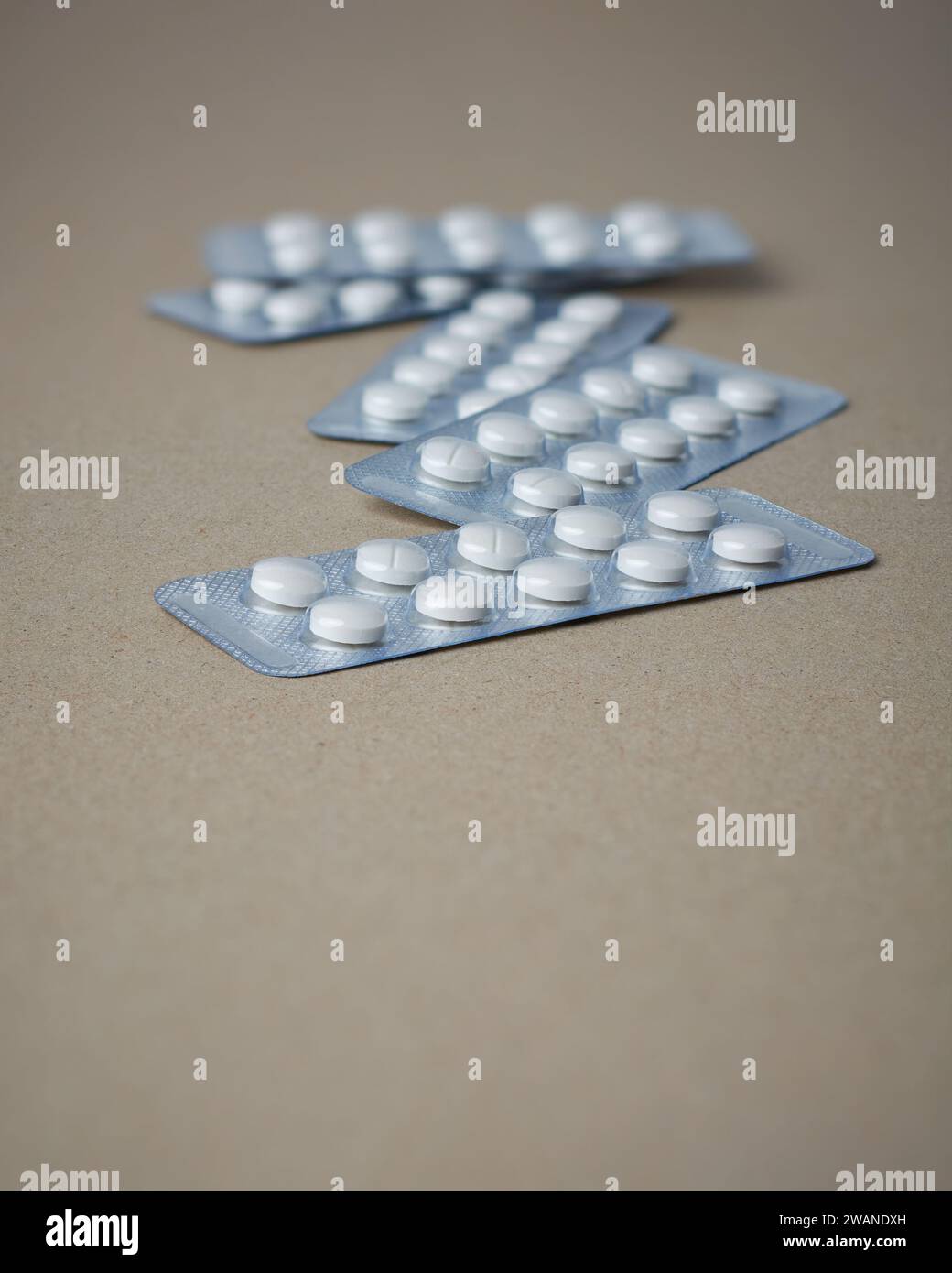 scattered white color tablets in blister packs, medical drugs for allergies, antibiotic, pain relievers, packages for tablets isolated on brown Stock Photo