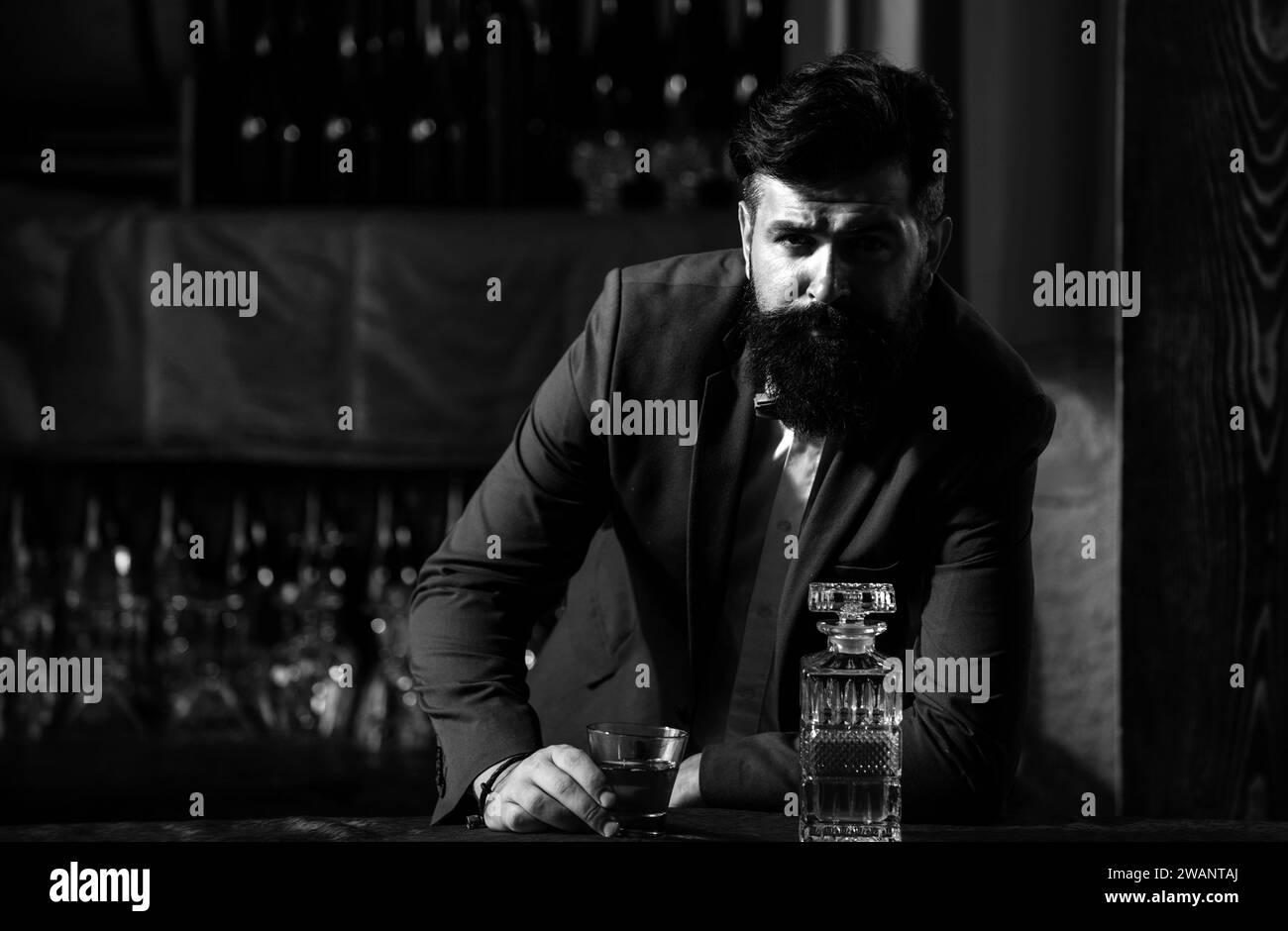 Barman luxury beverage concept. Man with beard holds glass with alcohol in bar. Waiter bartender in vintage vest with whiskey or scotch on tray. Stock Photo