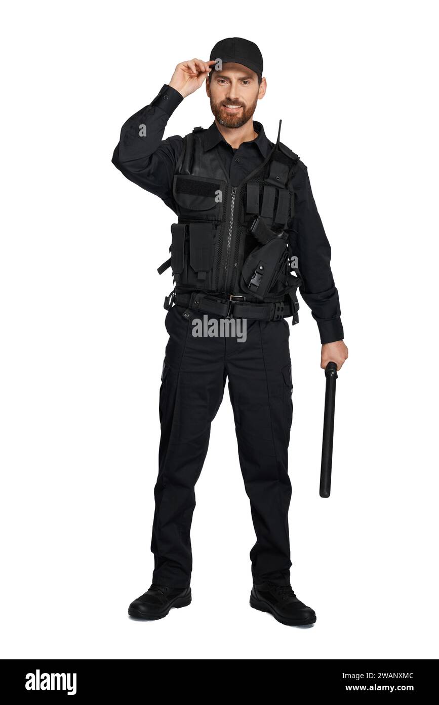 Smiling caucasian police officer in uniform standing with baton indoors. Front view of bearded cop with truncheon adjusting police cap, isolated on white studio background. Concept of work, outfit. Stock Photo
