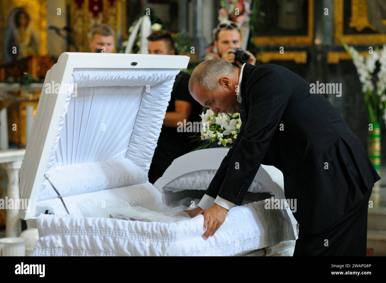Burial service in a church: man dressed in black mourning costume giving his last farewell to the late in white coffin. Funeral of peoples deputy Irin Stock Photo