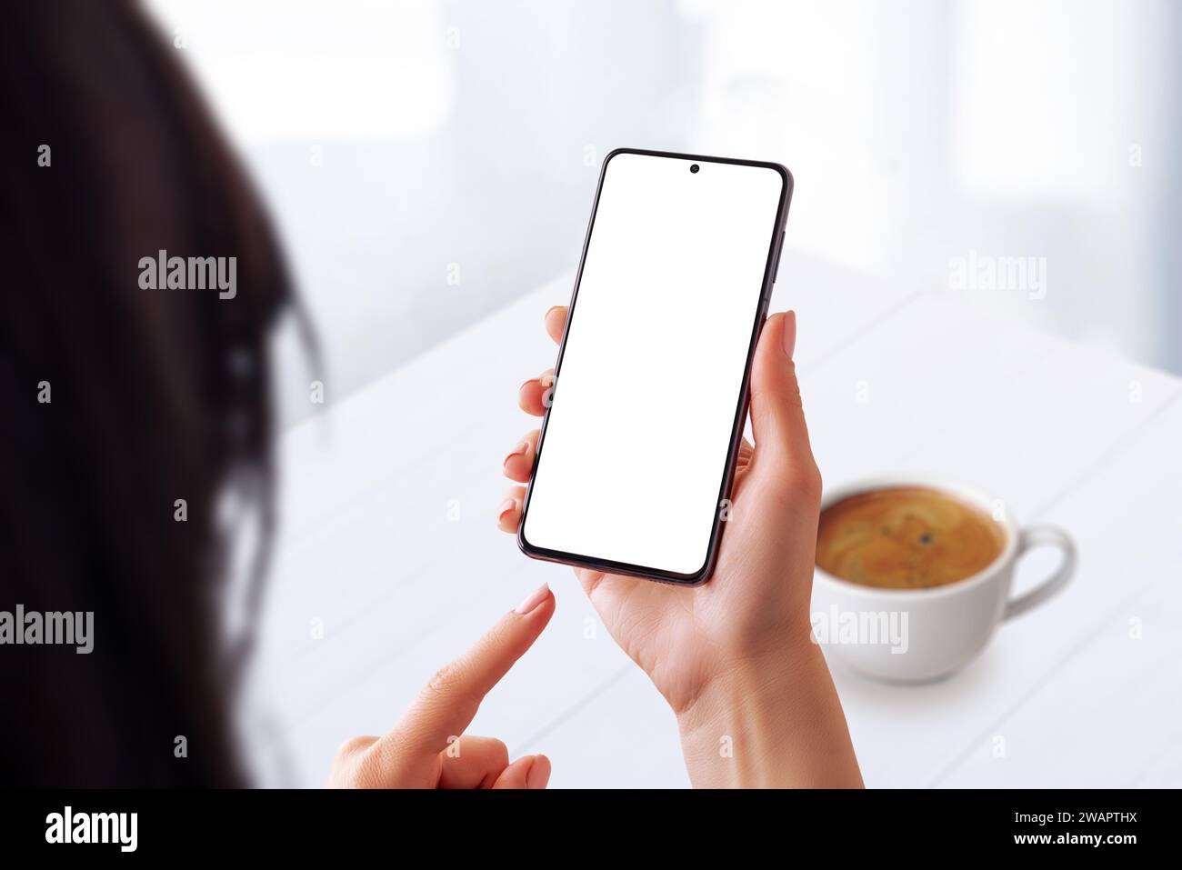 Woman in a coffee shop using a smartphone with an isolated screen for mockup. Ideal for showcasing mobile usability in a casual coffee time setting Stock Photo