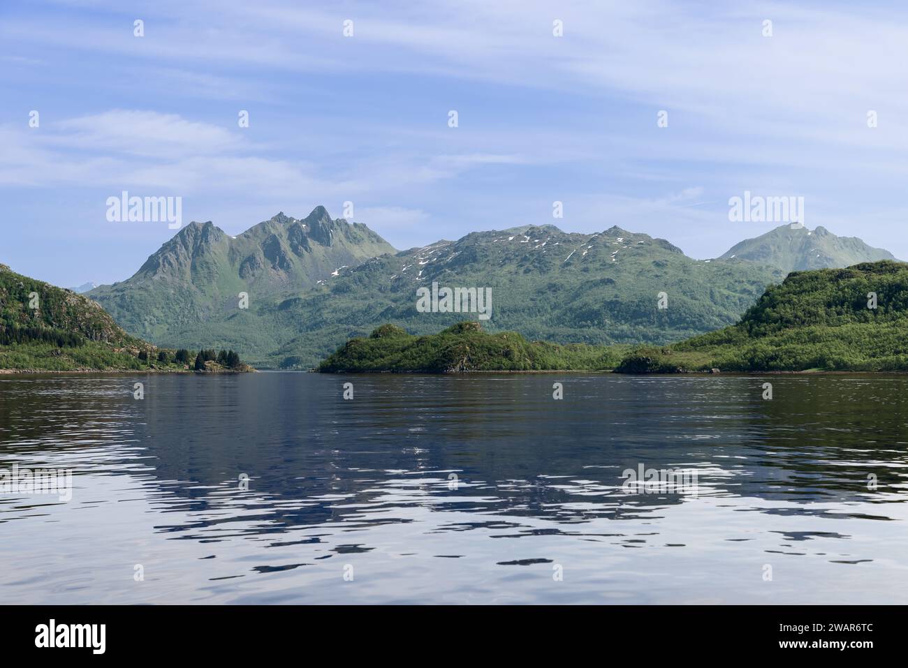 The serene fjord waters create a mirror image of the verdant Lofoten peaks under a clear sky, a testament to the untouched beauty of the Arctic Stock Photo