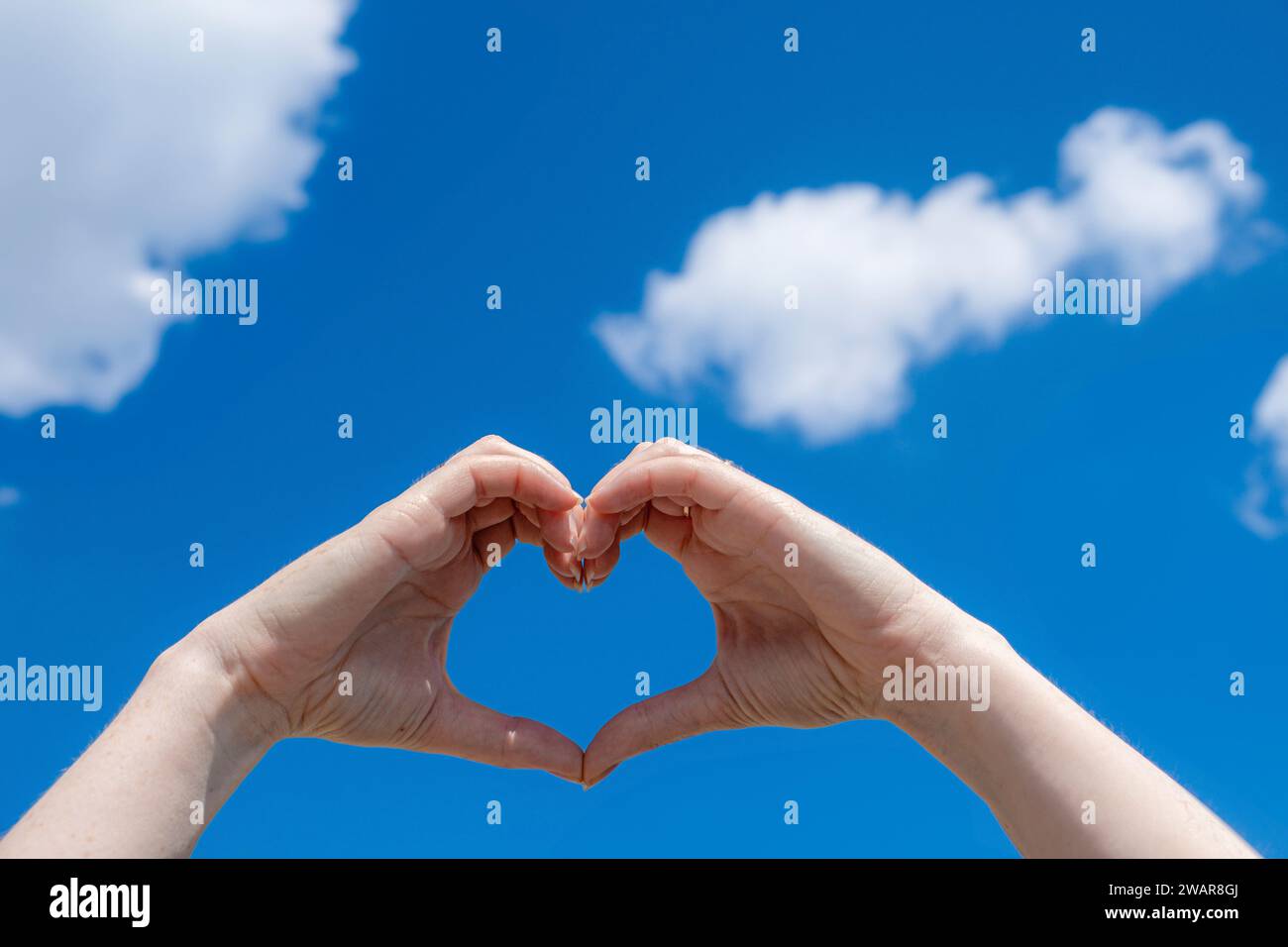 the girl shows a heart with her hands against the background of the sky Stock Photo