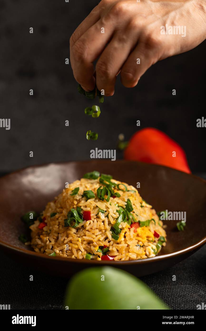 Hand adding the last ingredients to a Peruvian dish called Arroz chaufa. Stock Photo
