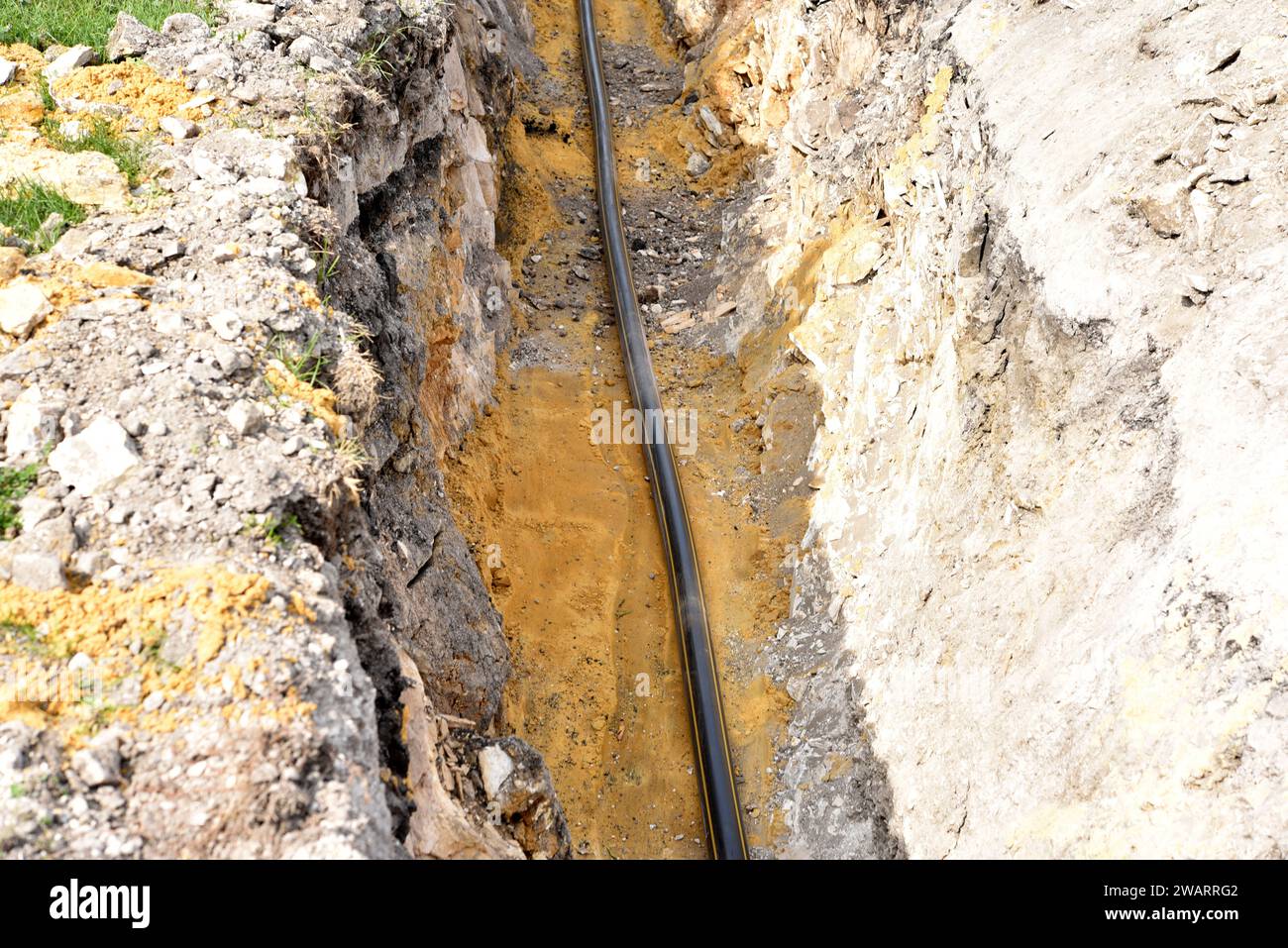 A plastic black gas pipe at the bottom of the trench. A dug trench for