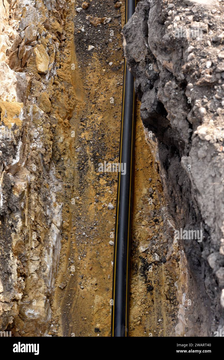 A plastic black gas pipe at the bottom of the trench. A dug trench for