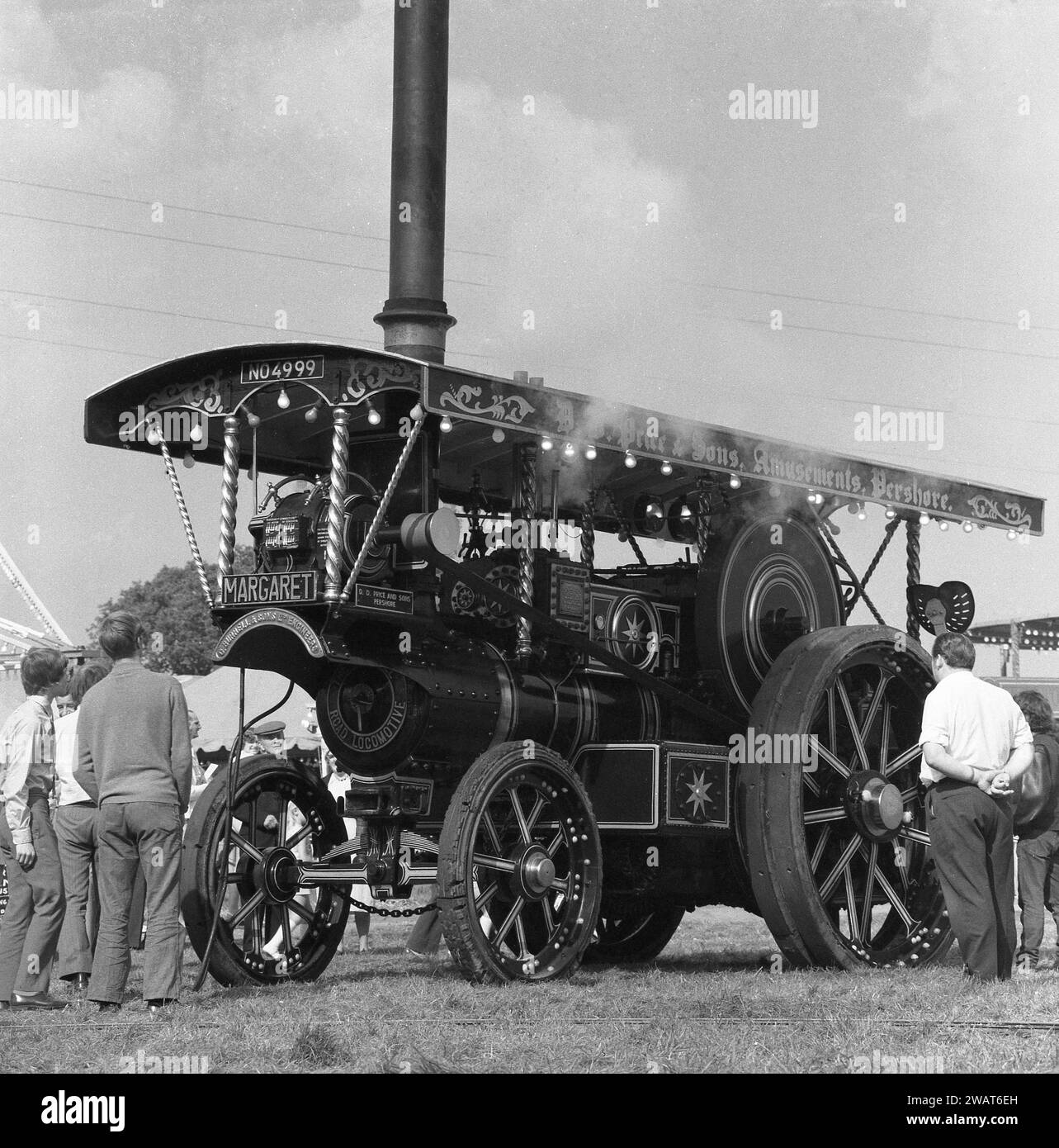 1970, historical, outside at a steam fair, visitors looking at the steam engine, 'Margaret', England, UK, built in 1922 and known as a Showmans Road Locomotive.  Maker's nameplate on front; C. Burrell & Sons Ltd, England. Number plate is NO 4999. Founded in 1770 and based at Thetford, Norfolk, Charles Burrell & Sons were leading builders of steam traction engines and related machinery and traded until the late 1920s, when the internal combustion engine became a more effective alternative to steam power. Stock Photo