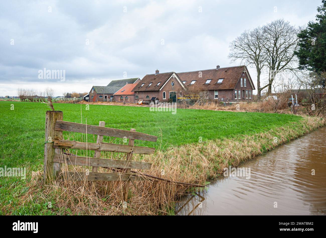 Idyllic image of a wooden fence near a ditch and old farmhouse in the Dutch landscape near Waddinxveen. Stock Photo