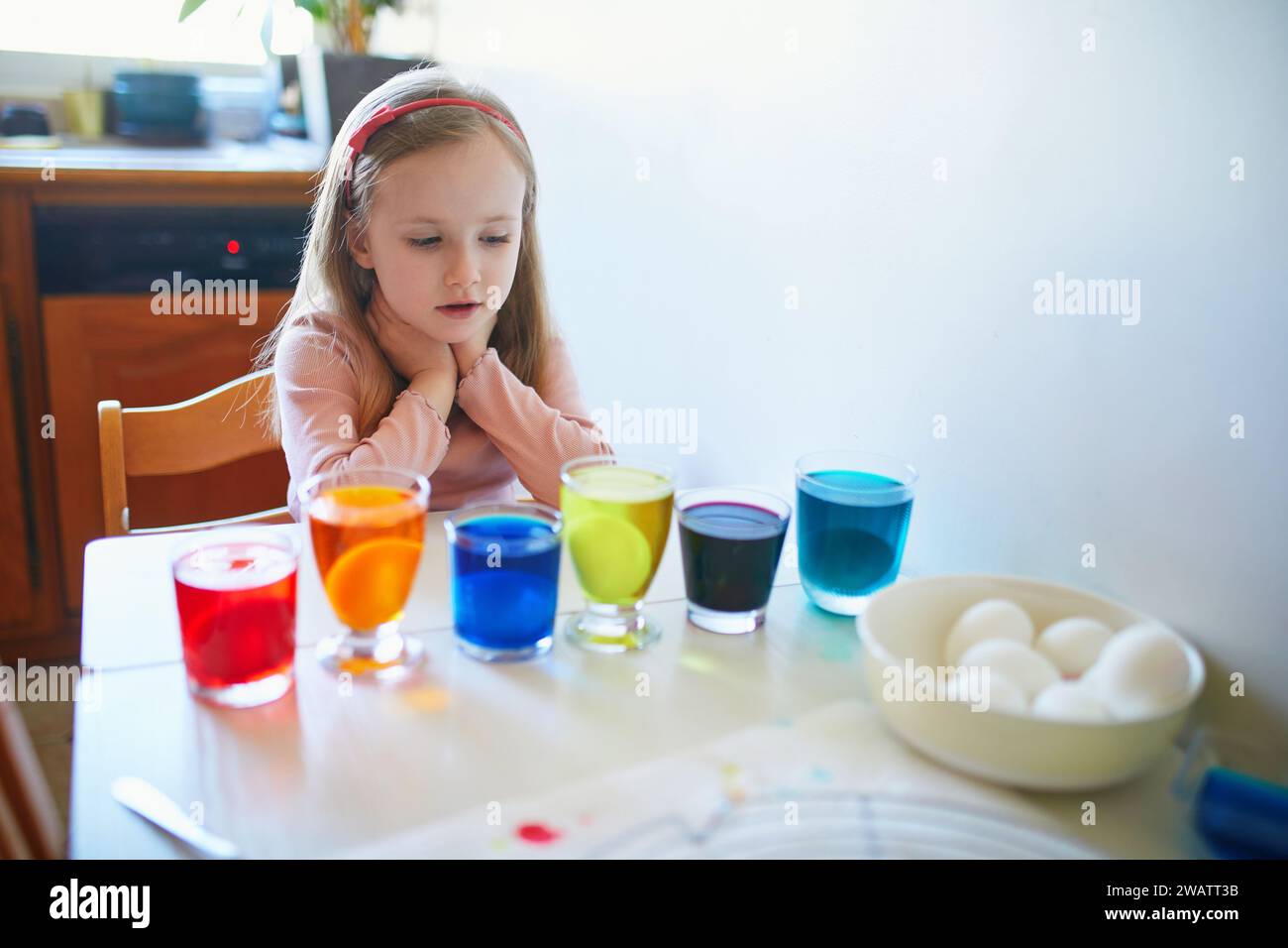 Adorable preschooler girl dyeing Easter eggs at home. Child painting colorful eggs for Easter hunt. Kid getting ready for Easter celebration. Family t Stock Photo