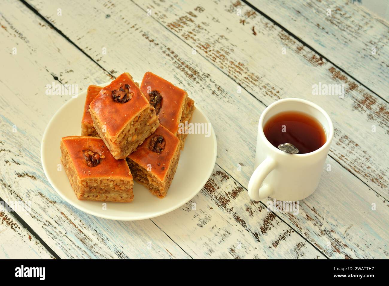 A cup of hot tea and a plate with delicious oriental baklava on a light wooden table. Close-up. Stock Photo