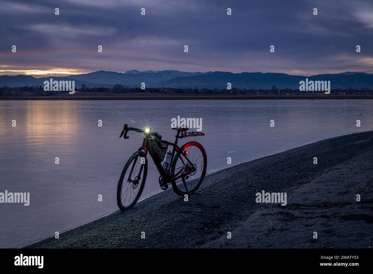 gravel bike on a shore of a frozen lake with distant view of Rocky Mountains, winter dusk in northern Colorado Stock Photo