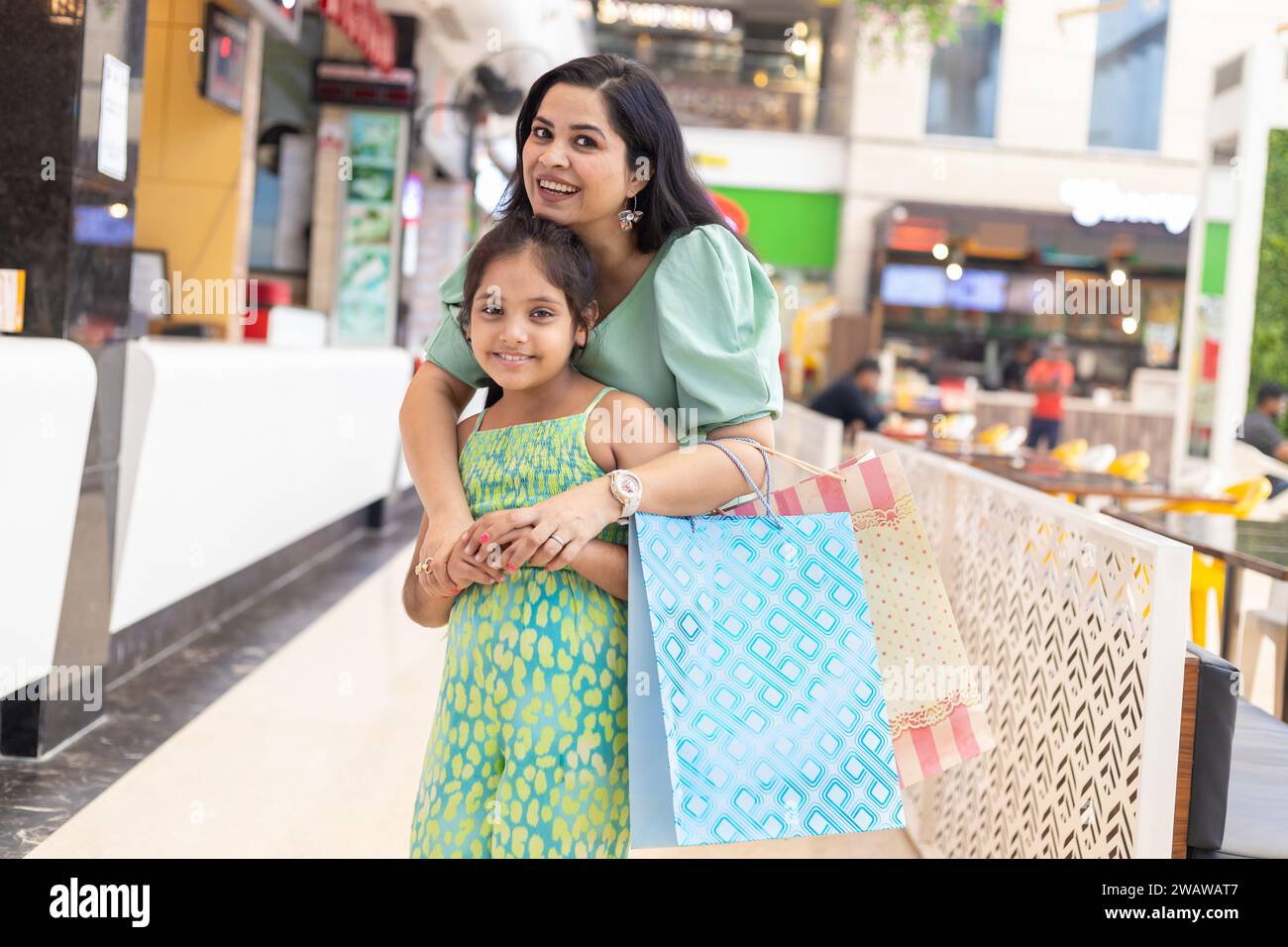 Happy indian mother and daughter standing in shopping mall holding hands of each other. shopping people concept. Stock Photo