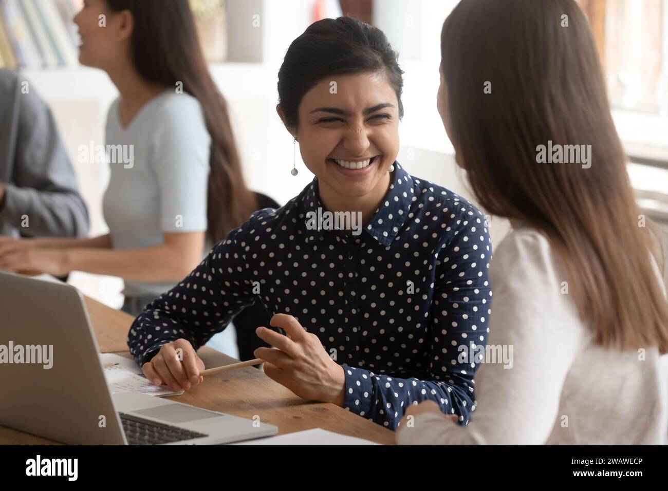 Overjoyed multiethnic female students laugh cooperating at project Stock Photo