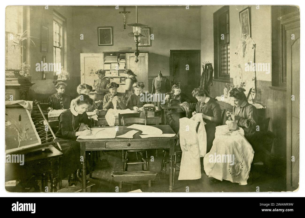 Original Edwardian postcard of young women in a Christian Catholic classroom with sewing, embroidery in a  needlework room at relgious school or convent for young ladies (there is a shrine to Our Lady.) The girls would have been trained in all aspects of running a household. Postcard dated / posted 1908, London, U.K. Stock Photo