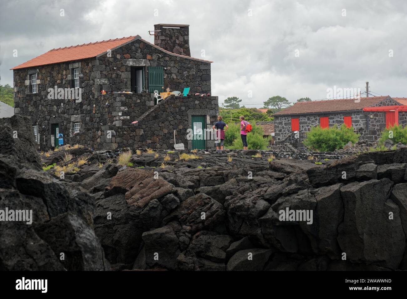 People standing next to a stone house on lava rock under an overcast sky, North Coast, Santa Luzia, Pico, Azores, Portugal Stock Photo