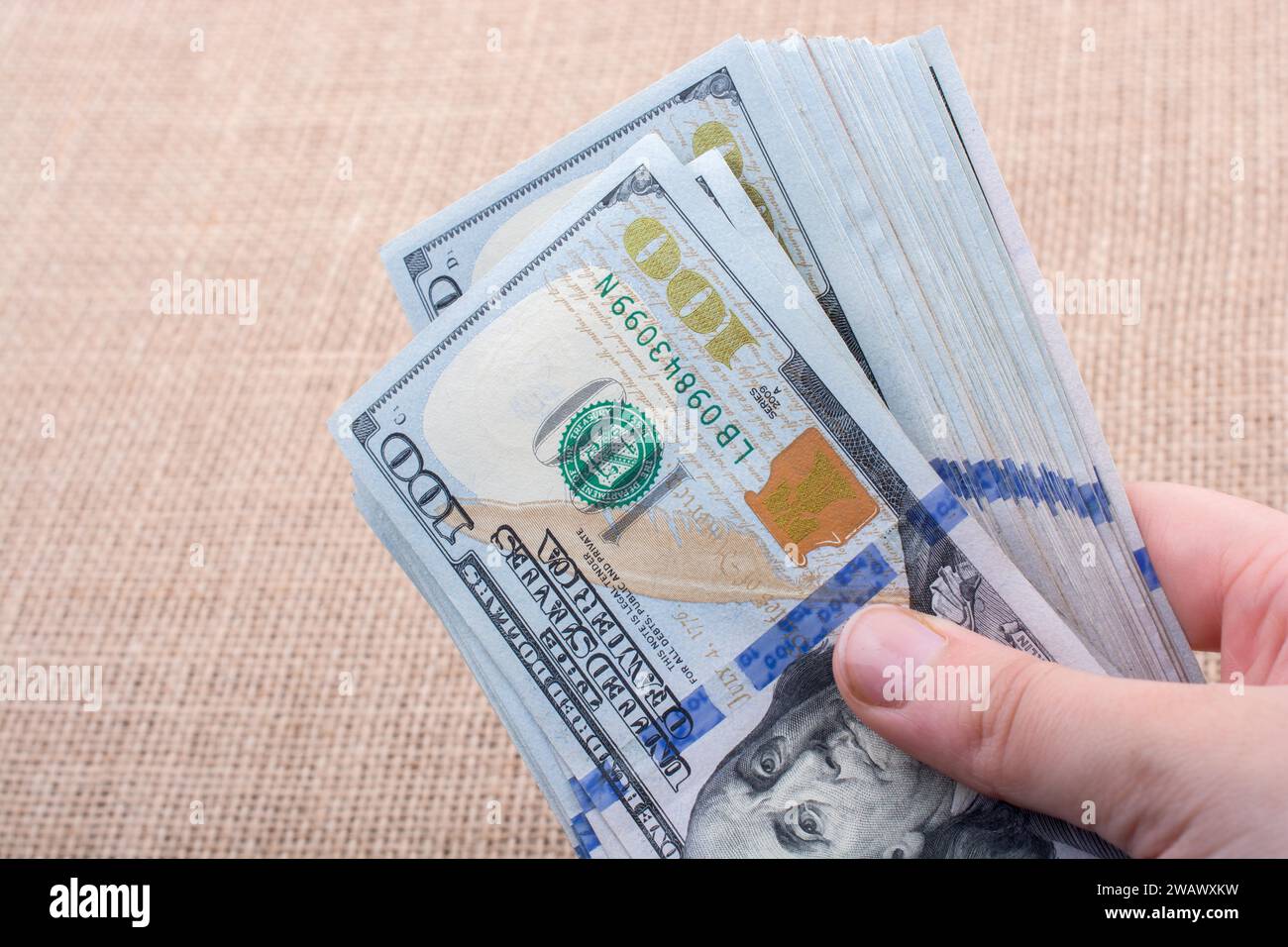Hand holding banknote bundle of US dollar on a linen canvas background ...
