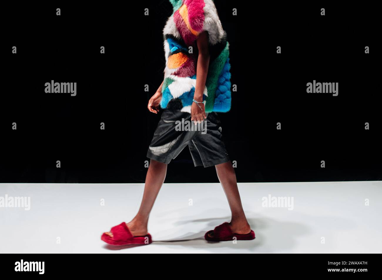 Part of a female figure dressed in a black shorts and fur coat walking on black background. Stock Photo