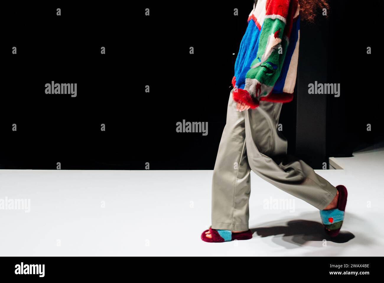 Part of a female figure dressed in a gray pants and fur coat walking on black background. Stock Photo