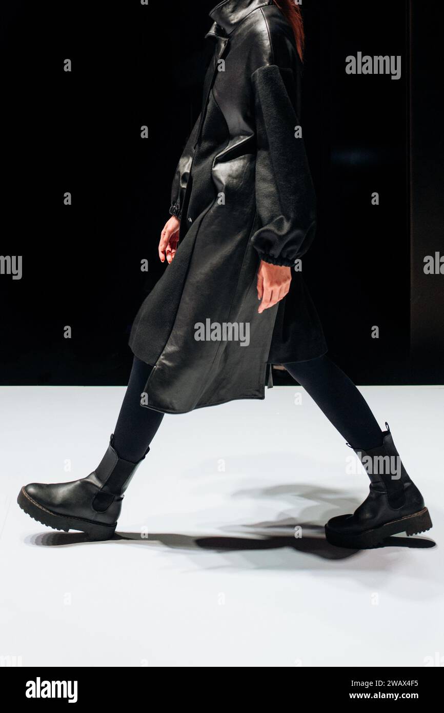 Female figure dressed in a black leather outfit walking on black background. Stock Photo