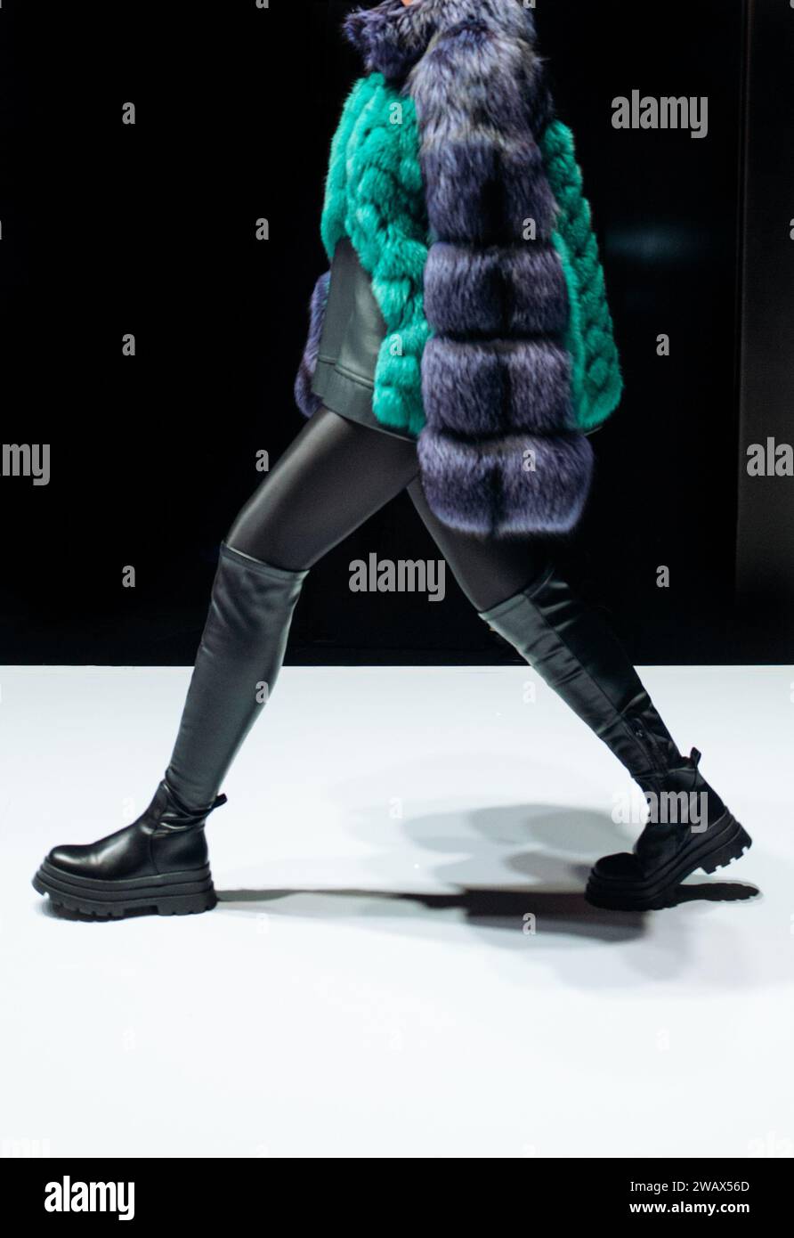 Female figure dressed in a fur coat and black leather boots walking on black background. Stock Photo