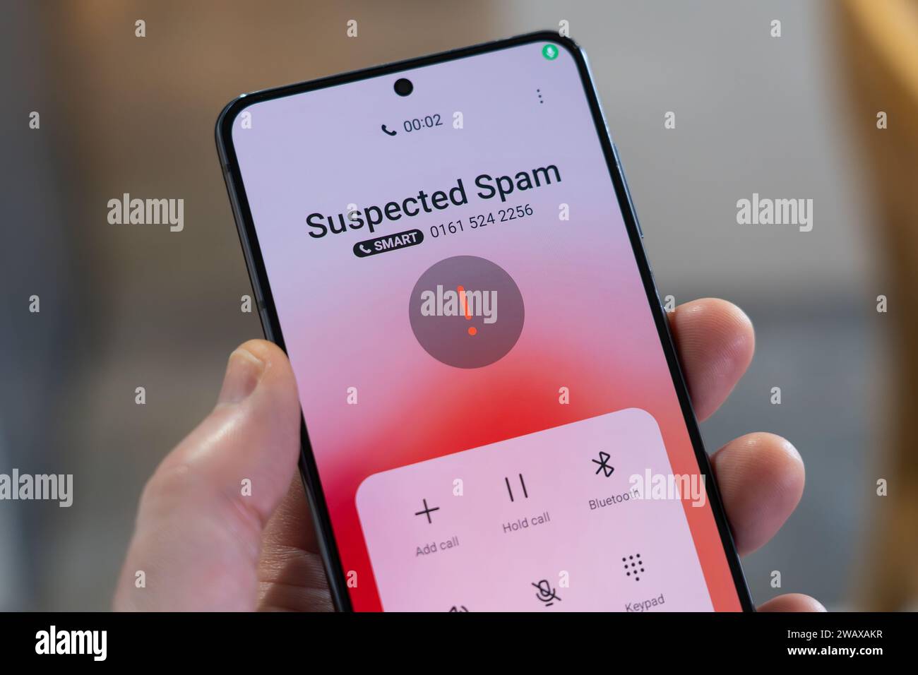 A hand holding a smartphone with an incoming call identified as suspected spam, UK. Theme: scam calls, fraudulent calls, cold calling, cold calls Stock Photo